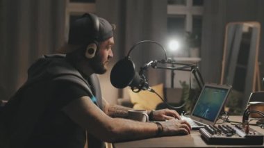 Evde oturup mikrofona konuşan, kulaklıklı neşeli sakallı adamı canlı yayında birinci şahıs nişancı video oyunu oynarken görüntülemek.