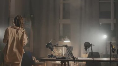 Stüdyo ışıklarıyla aydınlatılmış, karanlık oturma odasındaki masada oturan, kahveli, neşeli bir adamla bir kadının orta boy fotoğrafı. Konuşuyorlar ve podcast 'i kaydetmeye hazırlanıyorlar.