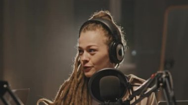 Rastalı, gülümseyen ve mikrofona konuşan mutlu genç bir kadının podcast ya da radyo programı sunarken çekilen görüntüsü.