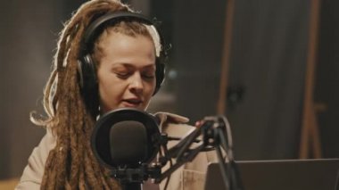 Rastalı, kulaklık takan, dizüstü bilgisayarı olan ve radyo programı ya da podcast sunarken mikrofona konuşan genç bir kadının görüntüsü.