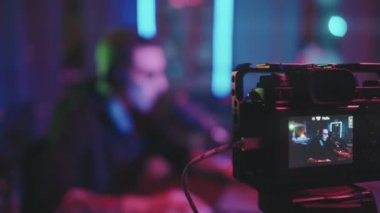Oturma odasındaki masada oturan gözlüklü genç adamın yavaşlığını neon ışıklarla aydınlatıp dizüstü bilgisayar veya podcast 'te video oyunu oynarken kendini kameraya çekmesini izlemek.