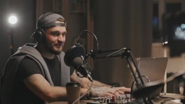 Kulaklıklı neşeli sakallı adamın görüntüsü. Masada oturuyor ve mikrofona konuşuyor. Tanımlanamayan yardımcı sunucuyla podcast yaparken.