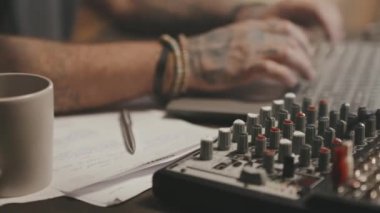 Ses mikserine, notalara ve bir fincan kahveye odaklanarak yakın çekim yapıyorum. Dizüstü bilgisayarda yazan tanınamayan erkek podcast sunucusu veya müzik yapımcısı