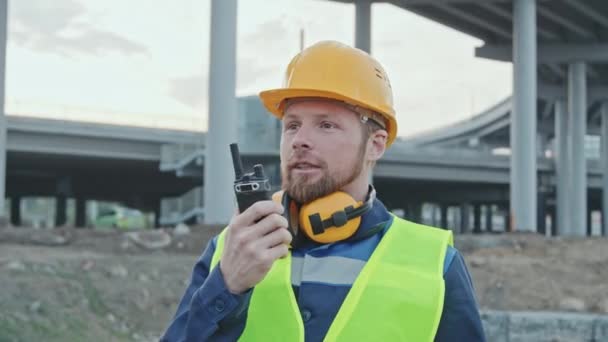 Tracking Shot Male Construction Site Foreman Standing Talking Walkie Talkie — Vídeos de Stock