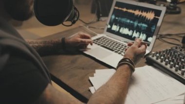 Masada oturan ve mikrofona konuşan tanınmayan bir adamın elleri yavaş çekimde çevrimiçi radyo programı ya da podcast 'i kaydederken.