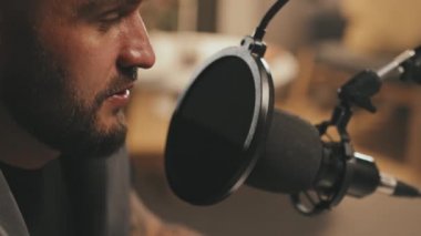 Podcast ya da radyo programı sırasında mikrofona konuşan sakallı bir gencin yakın plan görüntüsü.