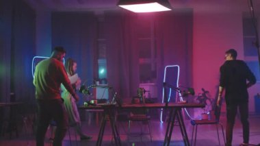 Oturma odasına neon ışıklarla aydınlanan ve podcast 'lerini kaydetmeye hazırlanan üç gencin orta ölçekli çekimi.