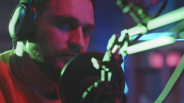 Sakallı, kulaklık takan ve mikrofona podcast ya da radyo programında konuşan genç adamın yakın plan fotoğrafı.
