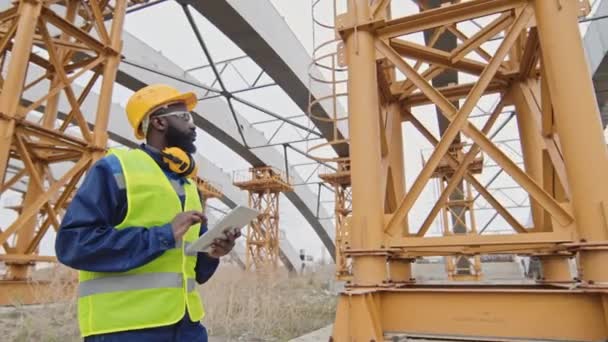 Sledovací Záběr Afroamerického Vedoucího Stavby Bezpečnostní Vestě Tvrdé Čepici Pomocí — Stock video