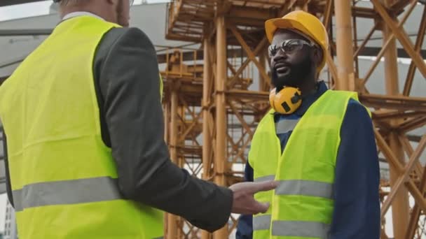 足場と建設の横で会話をし 合意に手を振るサイトの監督者とフォアマンの低い角度 — ストック動画