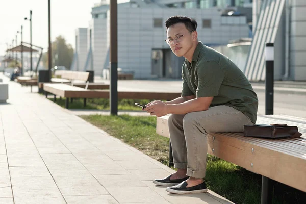 Jonge serene zakenman zittend op een bankje in de straat — Stockfoto