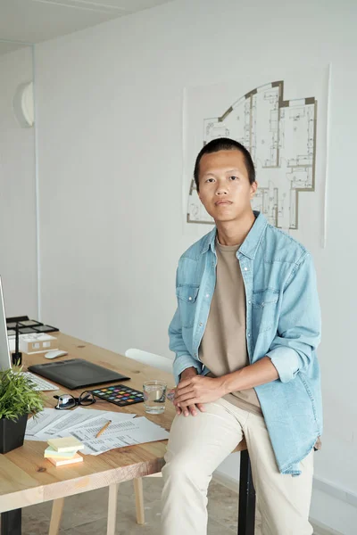 Contemporary young architect sitting on table against sketch on wall — Stock Photo, Image