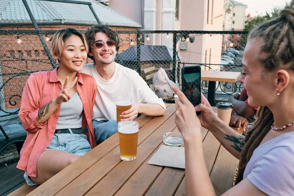 Feliz joven pareja posando para su amigo con teléfono inteligente —  Fotos de Stock