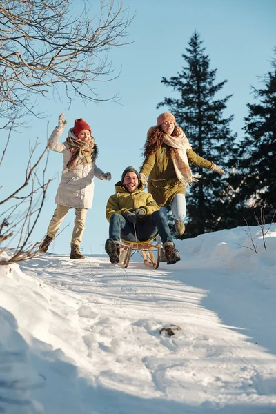 Two cheerful females and happy young man riding sledge — Stock Photo, Image