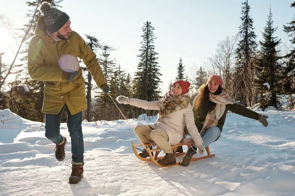 Two happy girls laughing while young man pulling sledge — Stock Photo, Image