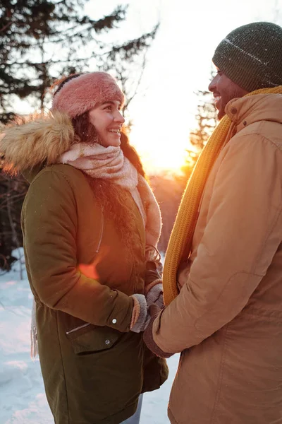 Jóvenes citas sonrientes en ropa de invierno mirándose mientras se agarran de las manos — Foto de Stock