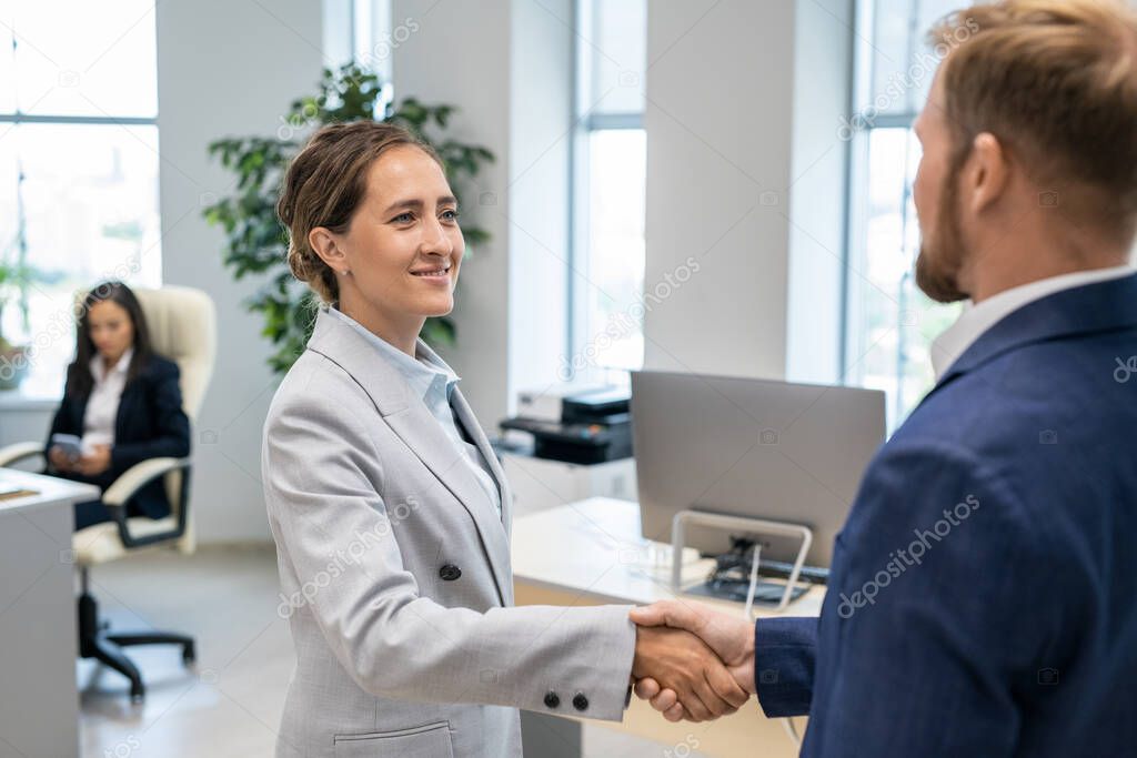 Two successful colleagues in formalwear handshaking after signing contract