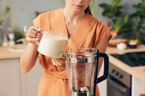 Mujer en vestido naranja vertiendo leche fresca en la licuadora eléctrica —  Fotos de Stock