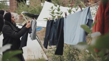 Soğuk rüzgarlı bir sabahta mülteci kampına çamaşır asan melez bir kadının orta boy fotoğrafı.