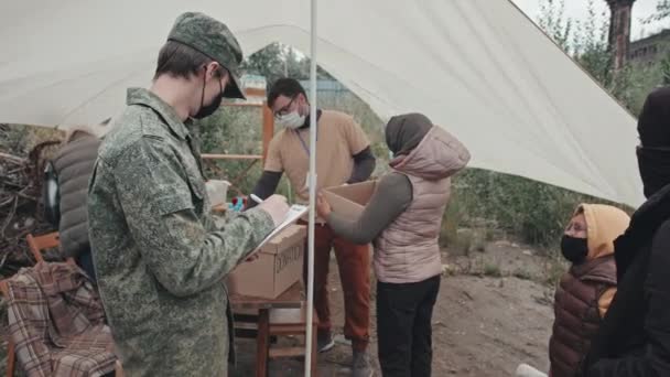 Tracking Shot Zespołu Pracowników Socjalnych Pod Namiotem Zapewniając Uchodźcom Bezdomnym — Wideo stockowe