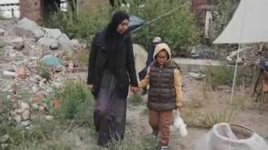 Diğer göçmenlerin soğuk bir günde yaşadıkları mülteci kampındaki çadırlarda oyuncak taşıyan kızıyla melez bir kadının fotoğrafını çekiyorum.