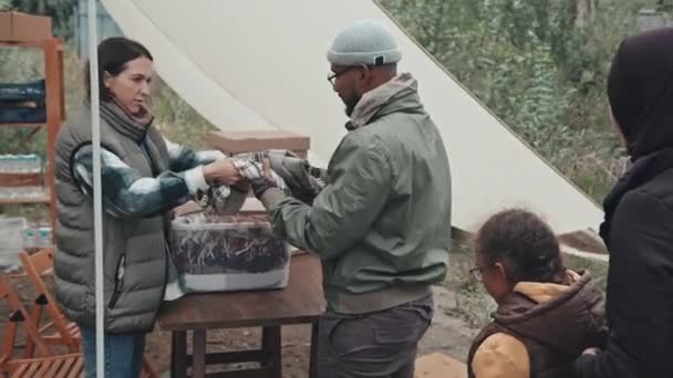 向帐篷城市生活条件恶劣的各种难民男子 妇女和儿童提供温暖毛毯的女性社会工作者中的一个镜头 — 图库视频影像