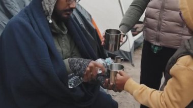 Mülteci çocuklar için metal bardaklara az miktarda su döken bir Arap 'ın el resmi. Çadır kenti sakinleri susuz.