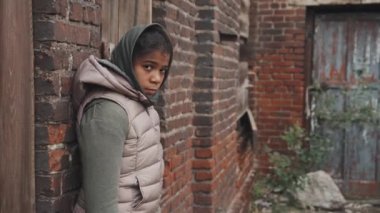 Terk edilmiş 11 yaşındaki Afro-Amerikan bir kızın orta boy portresi. Fakir bölgede, duvarın önünde kameraya bakıyor.