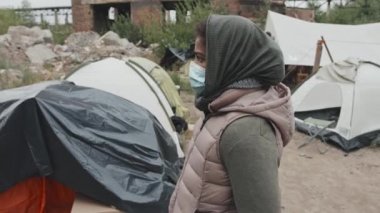 Soğuk bir günde çadır kentinde kameraya bakarken yüz maskesi takmış 11 yaşındaki Afro-Amerikan mülteci bir kızın orta boy yakın plan portresi.