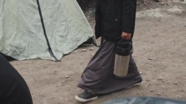 Siyah başörtüsü takan Müslüman bir kadının çeşitli evsiz ve mültecilerin yaşadığı fakir çadır şehri boyunca yürüdüğünü gösteren çekimler.