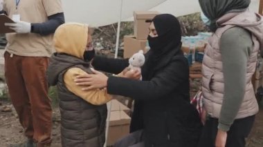 Siyahlı Müslüman bir kadının kızına baktığı, üzerine kalın giysiler giydiği fakir mülteci kampındaki çadırlarda yaşadığı orta boy bir fotoğraf.