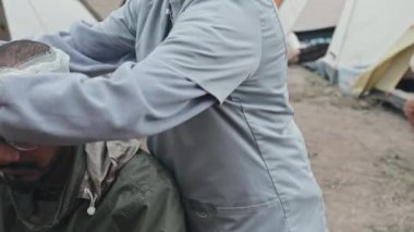 Tanınmayan bir kadın sağlık çalışanının çadır kentinde melez bir mülteciye ilk yardım yaptığı, kafasındaki yara bandıyla orta bölüm fotoğrafı.