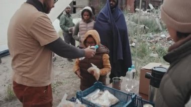 Sosyal hizmet görevlilerinin çadır kentte yaşayan evsiz veya mültecilere yardım ettiği, onlara yiyecek ve su sağladığı orta ölçekli bir fotoğraf.