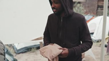 Afro-Amerikalı mültecinin sosyal hizmetler görevlilerinden sıcak giysiler alıp çadır kentinde yaşayan göçmenlere ya da evsizlere yardım ederken orta ölçekli bir fotoğrafı.