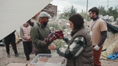 Mülteci kampında çadırın altında durup mülteci erkek, kadın ve çocuklara sıcak battaniye ve kıyafet veren sosyal hizmet görevlilerinden oluşan orta ölçekli bir fotoğraf.