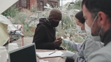 Koruyucu giysiler içinde tıbbi çalışanlardan oluşan orta ölçekli bir ekip, çadır şehrinde kötü koşullarda yaşayan siyahi mültecilere tıbbi yardım sağlıyor.