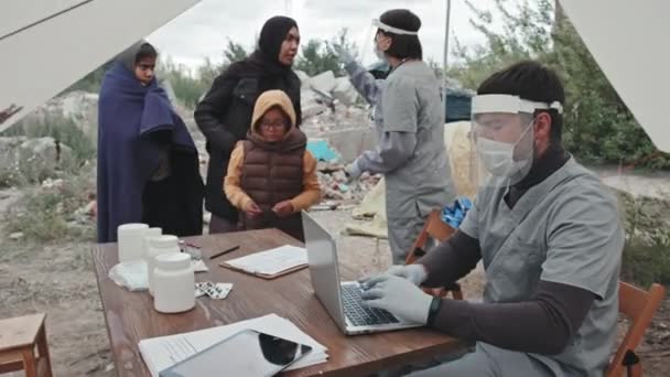Średnie Ujęcie Kobiety Pracownika Medycznego Odzieży Ochronnej Mierzącej Temperaturę Uchodźców — Wideo stockowe