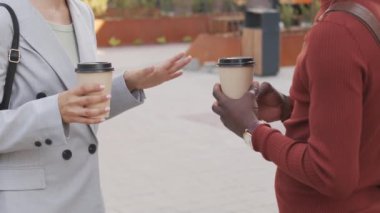 Orta kısımda, tanımadığımız iş ortaklarının açık havada el kol hareketleri yapan kağıt kahve fincanları tutan elleri görülüyor.