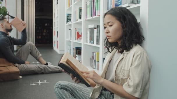 Medellångsam Bild Kvinnliga Asiatiska Universitetsstuderande Sitter Golvet Moderna Bibliotek Läsa — Stockvideo