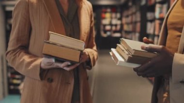 Tanınmayan zeki çoklu etnik giyimli çiftin orta bölüm yavaş çekimleri konuşma sırasında kütüphanede küçük bir yığın kitap tutuyor.
