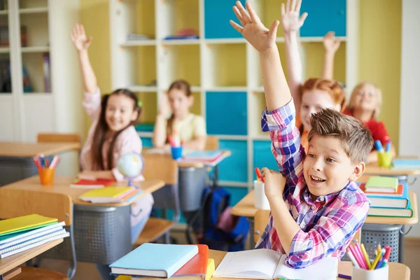 Pojke höja handen på arbetsplatsen med klasskamrater — Stockfoto