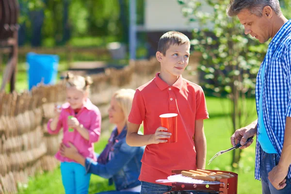 Man frying sausages and talking to son — Stock Photo, Image