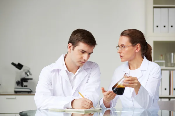 Scientists studying liquid oil in flask — Stock Photo, Image