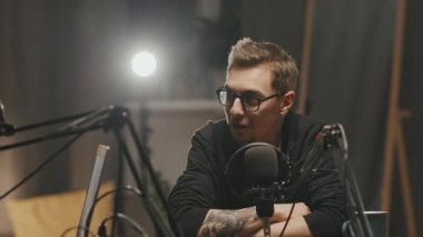 Gözlüklü neşeli bir gencin mikrofona konuşurken çekilen görüntüsü ya da kamera dışında iş arkadaşlarıyla röportaj yaparken.