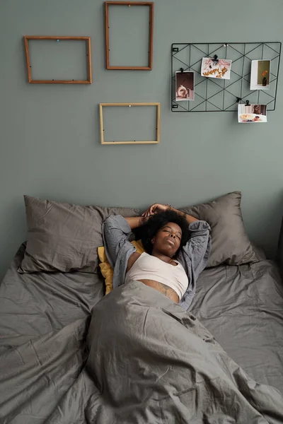 Νεαρή Αφρικανή ξαπλωμένη κάτω από κουβέρτα στο κρεβάτι — Φωτογραφία Αρχείου