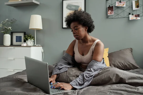Молода фрілансерка з ноутбуком сидить у ліжку та мережах — стокове фото
