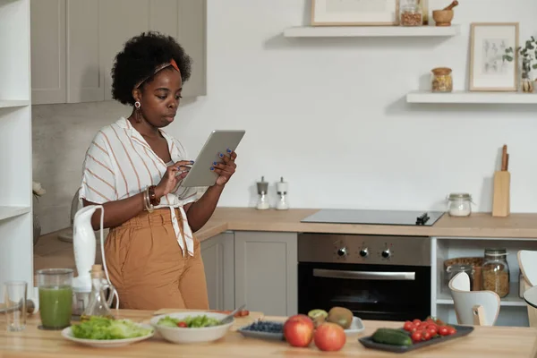 Νεαρή αφρικανική νοικοκυρά με tablet κοιτάζοντας μέσα από online συνταγές — Φωτογραφία Αρχείου