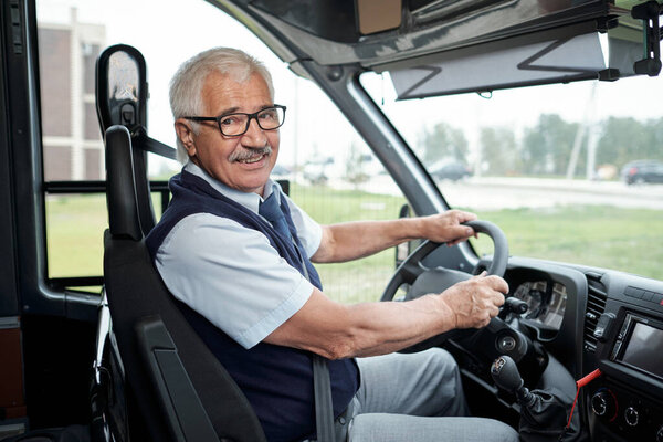 Happy aged driver of intercity bus holding by steering wheel