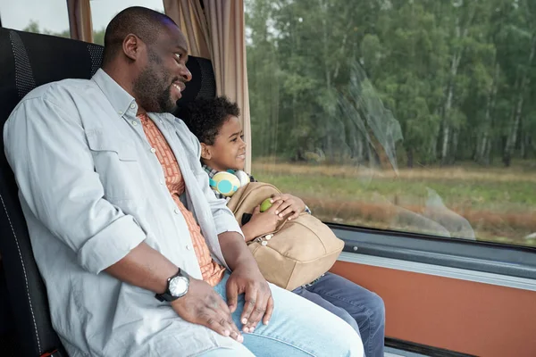 Młody ojciec i ładny syn z plecakiem patrząc przez okno autobusu — Zdjęcie stockowe