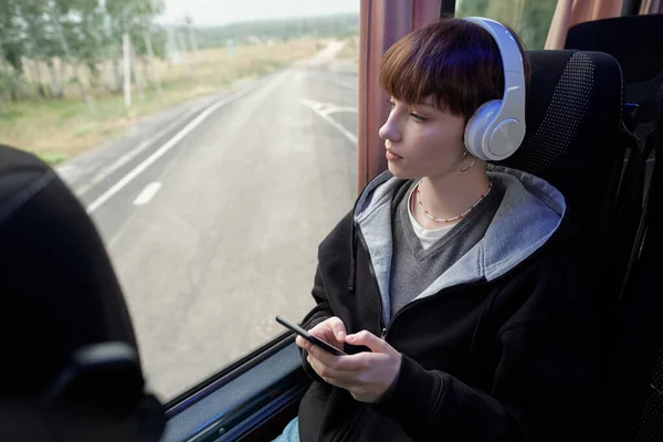 Young serene woman in headphones looking through window of bus — Stock Photo, Image